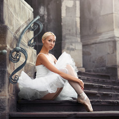 Looking thorough you. Portrait of a young ballerina sitting on an old stairway outdoors with her arms around her knees © serhiibobyk