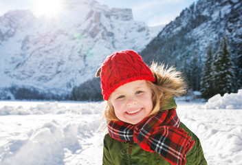 Fototapeta na wymiar Smiling child standing in the front of snowy mountains