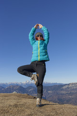 Pretty mid aged woman trekker relaxing, performing JOGA high in mountains on sunny winter day against  Mount Triglav, highest mountain in Slovenian  Alps, space for text