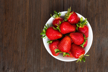 Fresh ripe strawberries in a simple white bowl, on dark wooden table