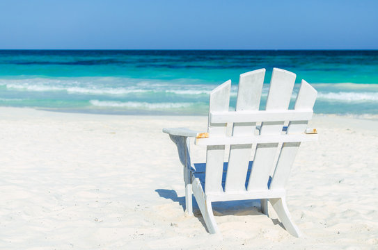 Tropical vacation beach resort sea view. Lonely beach white wooden chair over the background of turquoise sea and blue sky at exotic white sandy beach in the Caribbean sea