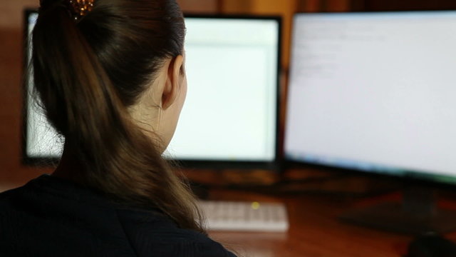 girl working in front of two monitors, rear view