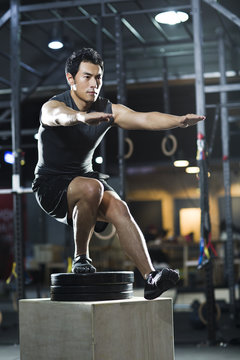 Young man doing box jump in crossfit gym