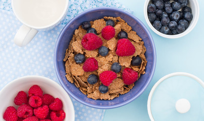 A healthy breakfast bowlful of cereals, raspberries and blueberries.  Looking down onto the table from above.