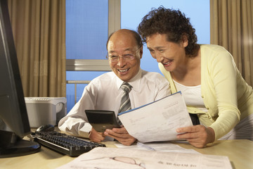 Businessman And Business Woman Smiling, Looking At Calculator