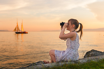 Outdoor portrait of a cute little girl playing by the lake on a nice warm evening, looking at the...