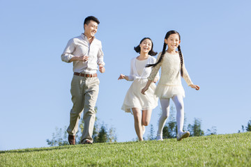 Naklejka na ściany i meble Joyful young family running in a park