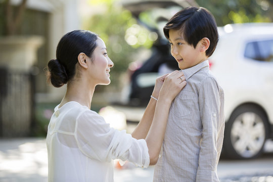 Mother buttoning shirt of her son outdoors
