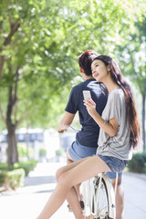 Fototapeta na wymiar Young woman sitting on boyfriend's bicycle with smart phone