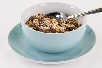 Blaue Müslischale auf blauem Teller gefüllt mit müsli, Rosinen und Nüssen.