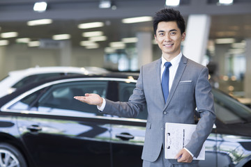 Confident salesman standing with new car in showroom