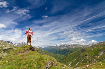 Young explorer in traditional clothing stands proud on top of a mountain in the Swiss Alps on a sunny summer day