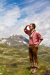 Fototapeta na wymiar Young explorer in traditional clothing looks out over the valley on top of a mountain in the Swiss Alps on a sunny summer day