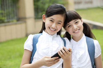 Excited schoolgirls in uniform with smart phone in school yard