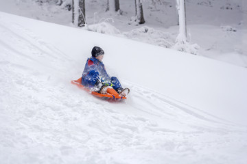 Fototapeta na wymiar Child on orange sled outdoors in snow 