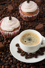 Chocolate cupcakes and cup of espresso on the coffee beans 