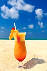 Glass of cocktail is on sandy coral  beach