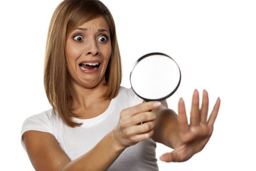 shocked young woman looking her nails with a magnifying glass