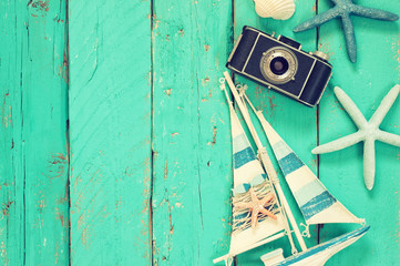 top view image of photo camera, wood boat, sea shells and star fish over wooden table
