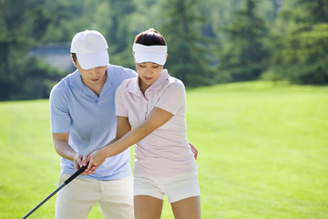 Young man teaching his girlfriend how to play golf