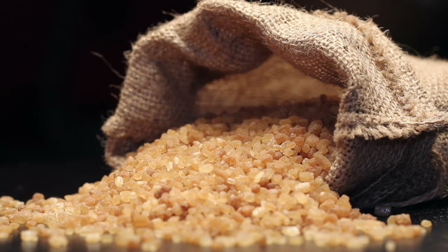 Brown sugar in gunny sack isolated on black, rotating