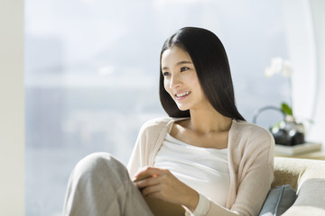 Happy young woman sitting on sofa with a book