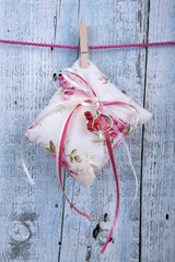 Decorative cushion with ribbons hanging on clothesline on old wooden background