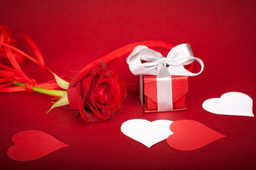 Rose, gift box and paper hearts on intense red background. Matte background. White elements.