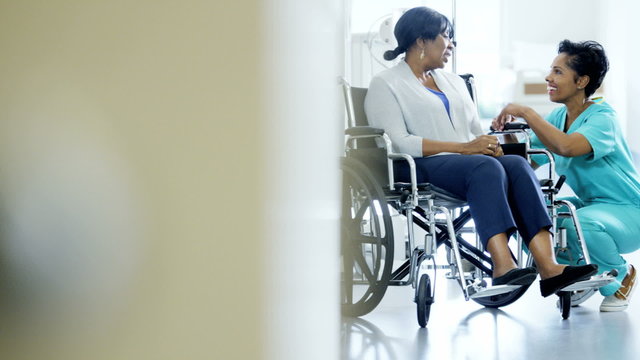 Portrait of African American female nurse and patient on wheelchair in hospital