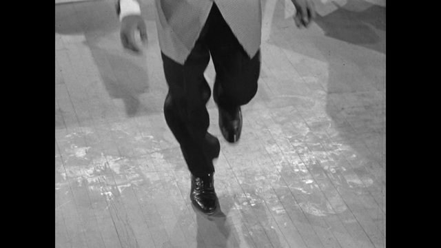 Front view of man tap dancing on wooden floor, 1950s
