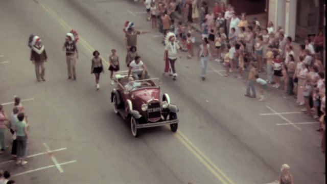 Men in vintage car waving towards spectators during parade