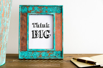 Vintage photo frame on wooden table with text THINK BIG