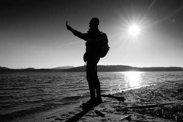 Man holding cellphone, taking picture of autumn sunset or sunrise in picturesque sea scenery