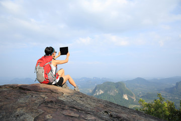 Obraz premium young woman hiker taking photo with digital tablet on mountain peak