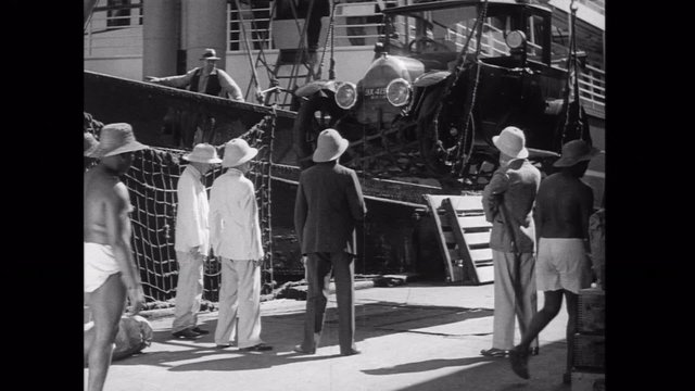Men watching car unloaded from ship to dock