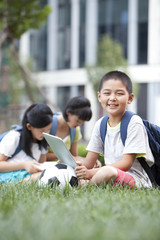 Schoolchildren sitting on the lawn with digital tablet