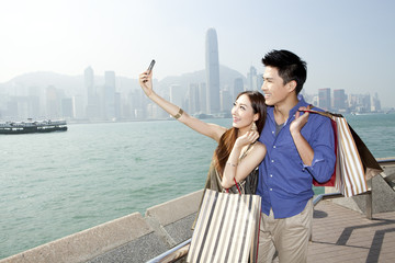 Fashionable young couple with shopping bags taking self-portrait pictures in Victoria Harbor, Hong Kong