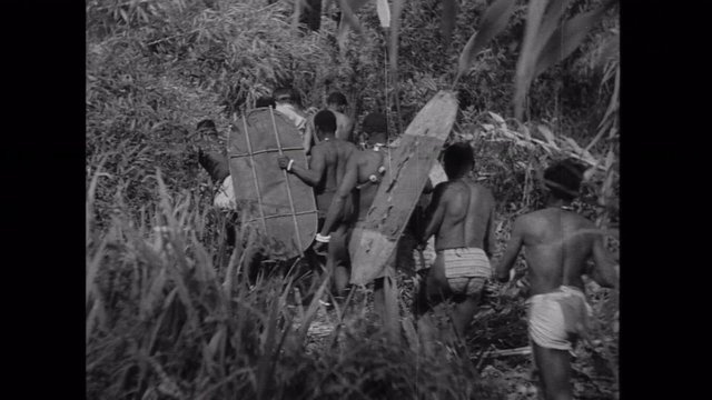 Rear view of tribesmen escorting captured man through jungle