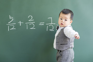 Cute baby doing mathematics on blackboard