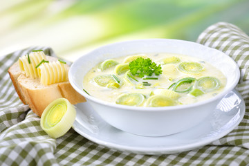 Vegetarische Lauch-Käse-Suppe in weißer  Suppenschale mit Butterbaguette vor softigem ...