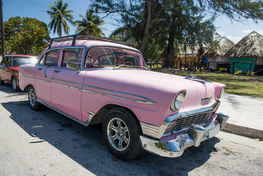 Amerykański zabytkowy różowy samochód na Kubie pod palmami w słoneczny dzień