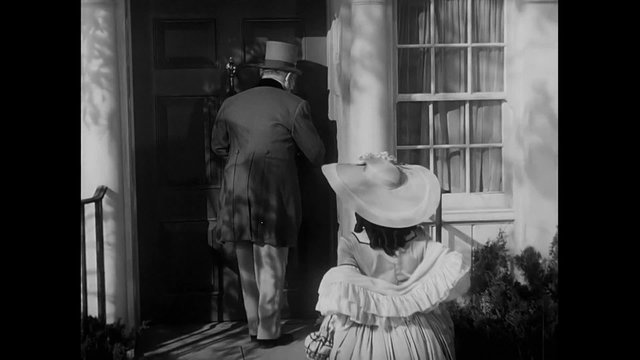 Rear view of couple dressed in 18th century clothing entering house, 1940s