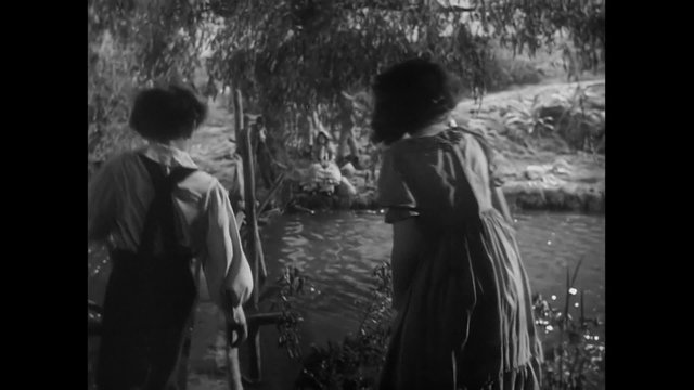 Young boy and girl walking next to river, 1940s