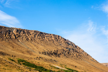 Rocky dry yellow cliff slope against light blue sky