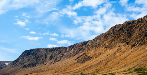 Rocky dry yellow cliff slope against light blue sky