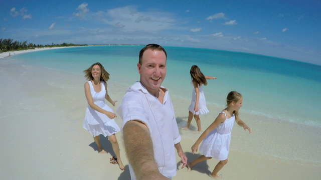 Video selfie of smiling carefree Caucasian family barefoot on beach 