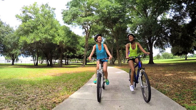 Young slim multi ethnic females riding bicycles in park