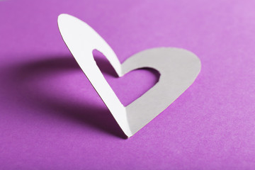 Cut out white paper heart on purple background