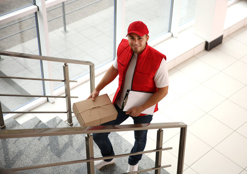 Delivery concept - postman in red uniform rising on stairs with package