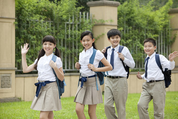 Obraz premium Cute schoolchildren in uniform waving at school yard